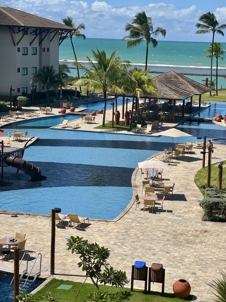 Área de lazer de resort infantil com piscina e coqueirais ao fundo.