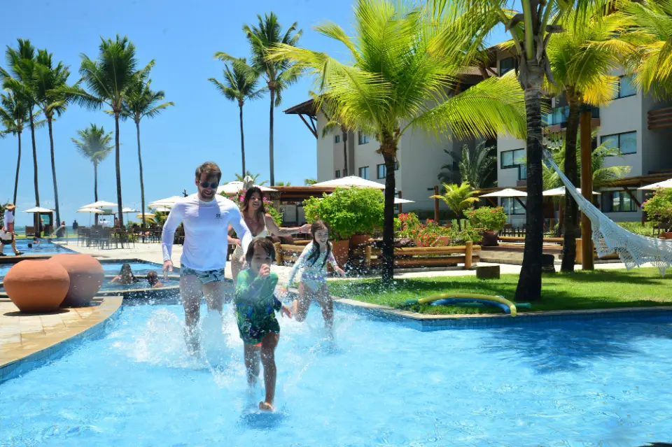Família corre de mãos dadas pela piscina do Samoa Beach Resort, entre coqueiros